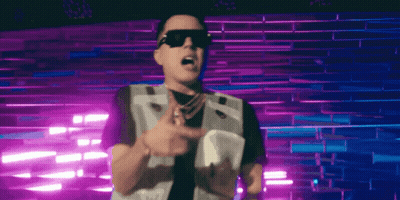 A Man Wearing Sunglasses And A Vest Stands In Front Of A Purple Wall GIF