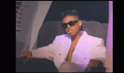 A Man Wearing Sunglasses And A White Jacket Is Sitting In A Chair . GIF