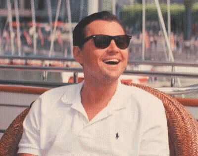 A Man Wearing Sunglasses And A White Polo Shirt Is Sitting In A Chair And Laughing . GIF