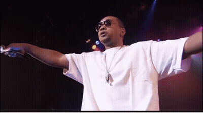 A Man Wearing Sunglasses And A White Shirt Holds A Microphone GIF