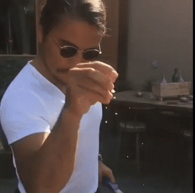 A Man Wearing Sunglasses And A White Shirt Holds Something In His Hands GIF