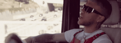 A Man Wearing Sunglasses And A White Shirt Is Driving A Car GIF