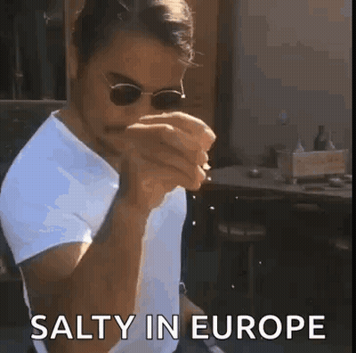 A Man Wearing Sunglasses And A White Shirt Is Eating A Sandwich While Sitting At A Table . GIF
