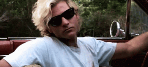 A Man Wearing Sunglasses And A White Shirt Is Sitting In The Driver 'S Seat Of A Car GIF