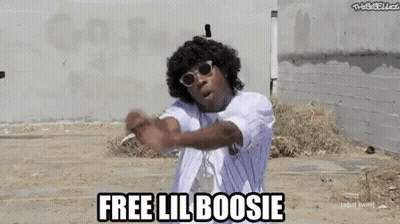 A Man Wearing Sunglasses And A White Shirt Is Standing In A Dirt Field And Says `` Free Lil Boosi '' . GIF