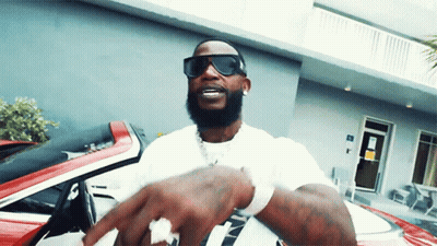A Man Wearing Sunglasses And A White Shirt Is Standing In Front Of A Red Car GIF