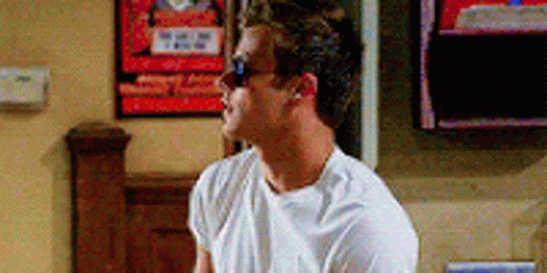 A Man Wearing Sunglasses And A White T-Shirt Is Sitting In Front Of A Tv . GIF