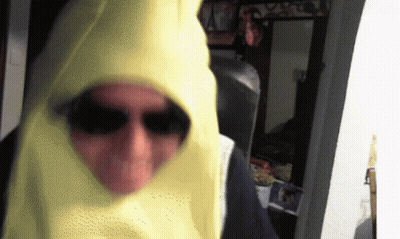 A Man Wearing Sunglasses And A Yellow Hood Is Standing In A Room GIF