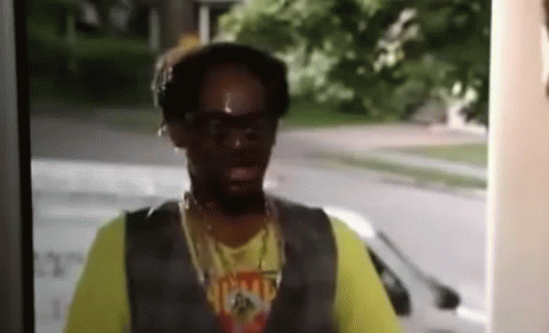 A Man Wearing Sunglasses And A Yellow Shirt With The Word Home On It Is Standing In Front Of A Door . GIF