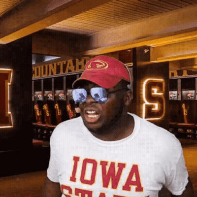 A Man Wearing Sunglasses And An Iowa Shirt Stands In A Locker Room . GIF