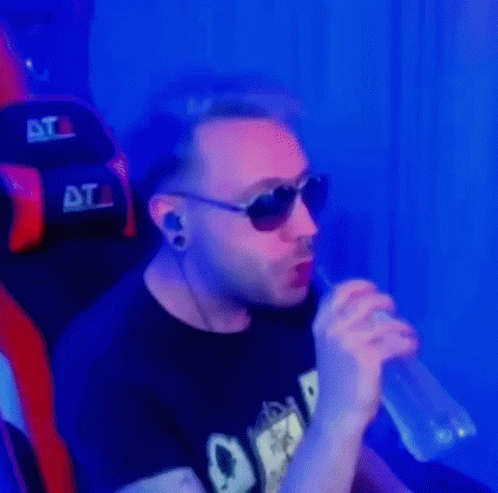 A Man Wearing Sunglasses And Ear Plugs Is Drinking From A Bottle While Sitting In A Chair . GIF