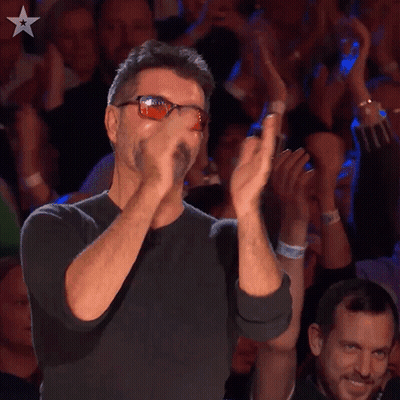 A Man Wearing Sunglasses Applauds In Front Of A Crowd Of People GIF