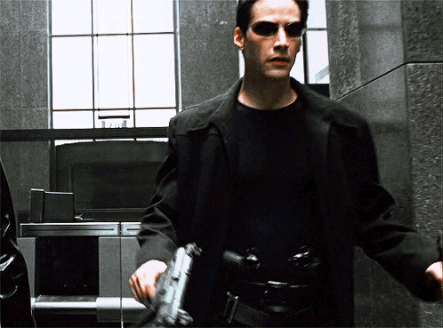 A Man Wearing Sunglasses Holds A Gun In His Hand GIF