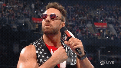 A Man Wearing Sunglasses Holds A Microphone In Front Of A Crowd And The Words Rawxxx Are Visible GIF