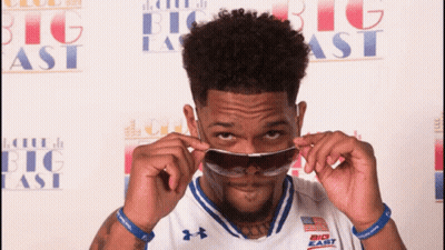 A Man Wearing Sunglasses In Front Of A Big East Banner GIF