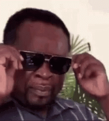 A Man Wearing Sunglasses Is Adjusting His Glasses And Making A Funny Face . GIF