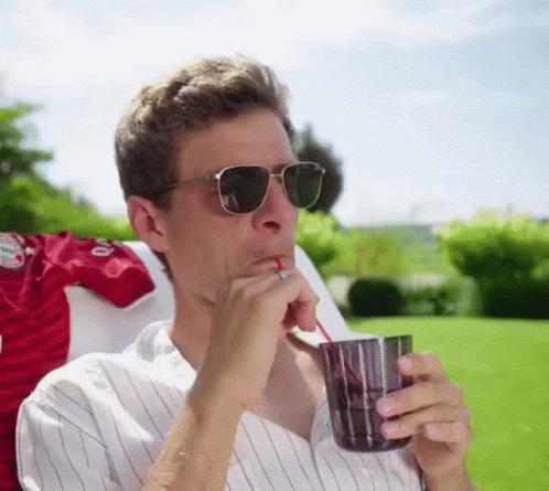 A Man Wearing Sunglasses Is Drinking From A Glass Through A Straw GIF