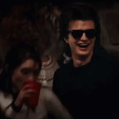 A Man Wearing Sunglasses Is Drinking From A Red Cup While A Woman Looks On . GIF