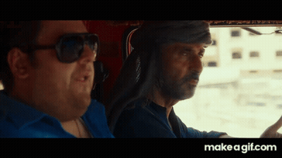 A Man Wearing Sunglasses Is Driving A Car Next To Another Man GIF