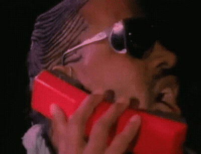 A Man Wearing Sunglasses Is Holding A Red Cell Phone To His Face . GIF