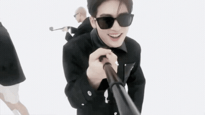 A Man Wearing Sunglasses Is Holding A Stick In His Hand While Standing Next To Another Man . GIF