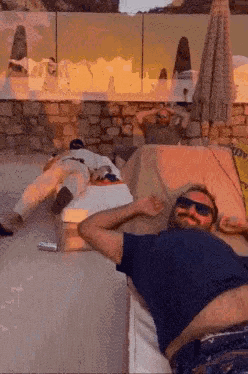 A Man Wearing Sunglasses Is Laying On A Couch With Another Man Laying On A Bed . GIF