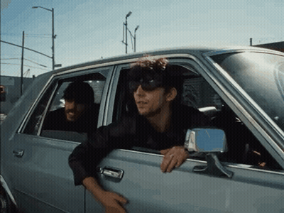 A Man Wearing Sunglasses Is Leaning Out Of A Car Window GIF