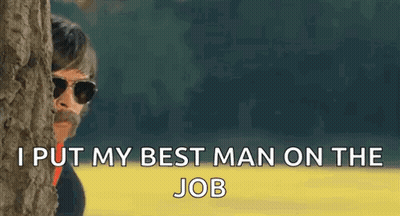 A Man Wearing Sunglasses Is Peeking Out From Behind A Tree . GIF
