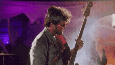 A Man Wearing Sunglasses Is Playing A Bass Guitar GIF