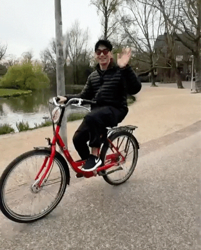 A Man Wearing Sunglasses Is Riding A Red Bike And Waving GIF