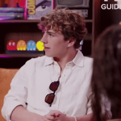A Man Wearing Sunglasses Is Sitting At A Table With A Sign That Says Guide GIF