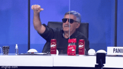 A Man Wearing Sunglasses Is Sitting At A Table With Two Red Cans Of Budweiser GIF