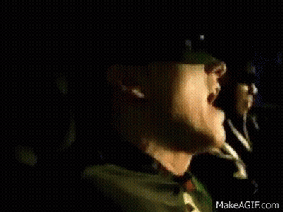 A Man Wearing Sunglasses Is Sitting In A Car Next To Another Man Wearing A Green Jacket . GIF