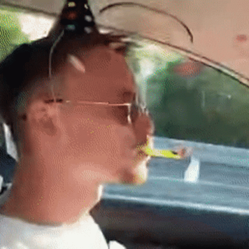 A Man Wearing Sunglasses Is Sitting In A Car With A Cigarette In His Mouth . GIF