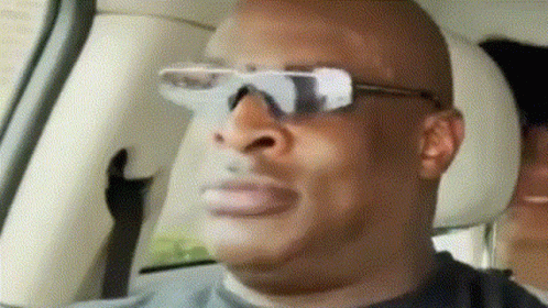 A Man Wearing Sunglasses Is Sitting In A Car With A Woman Behind Him GIF