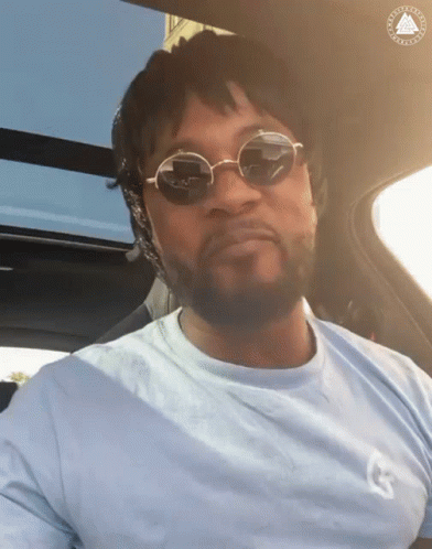 A Man Wearing Sunglasses Is Sitting In A Car With The Letter G On His Shirt GIF