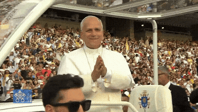 A Man Wearing Sunglasses Is Sitting In Front Of A Crowd With A Sign That Says ' Rio 2016 ' On It GIF
