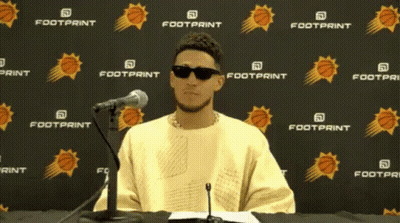 A Man Wearing Sunglasses Is Sitting In Front Of A Footprint Banner GIF