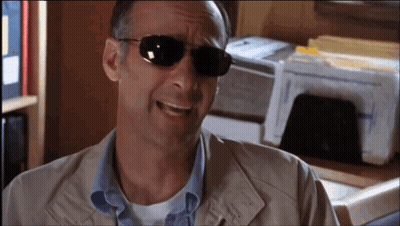 A Man Wearing Sunglasses Is Smiling In Front Of A Printer . GIF