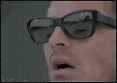 A Man Wearing Sunglasses Is Smoking A Cigarette And Looking At The Camera . GIF