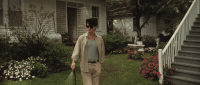 A Man Wearing Sunglasses Is Spraying The Grass In Front Of A House GIF