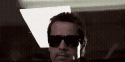 A Man Wearing Sunglasses Is Standing In A Dark Room . GIF