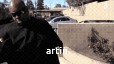 A Man Wearing Sunglasses Is Standing In Front Of A Brick Wall And The Word Artin Is On The Bottom GIF