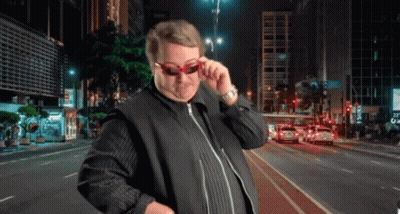 A Man Wearing Sunglasses Is Standing In Front Of A City Street At Night GIF