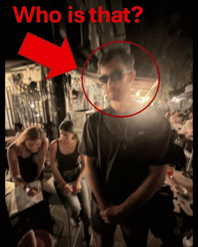 A Man Wearing Sunglasses Is Standing In Front Of A Group Of People With A Red Arrow Pointing To The Man 'S Face GIF
