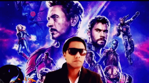 A Man Wearing Sunglasses Is Standing In Front Of A Movie Poster For The Avengers GIF