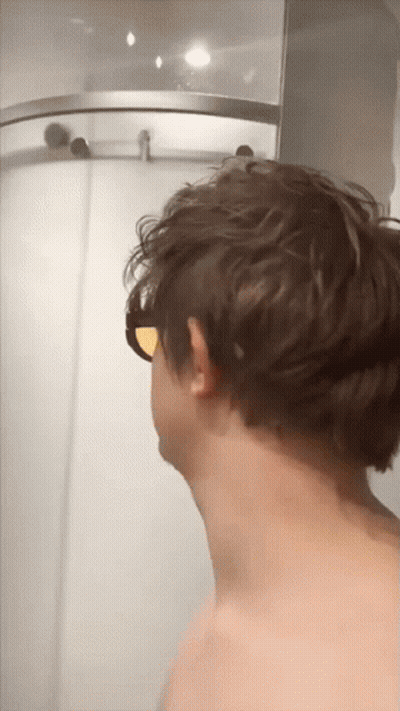 A Man Wearing Sunglasses Is Standing In Front Of A Shower GIF