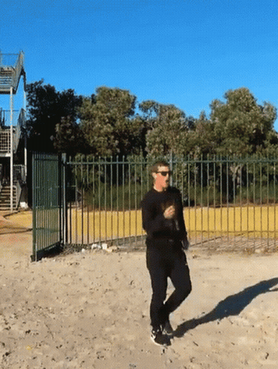 A Man Wearing Sunglasses Is Walking Across A Dirt Field GIF