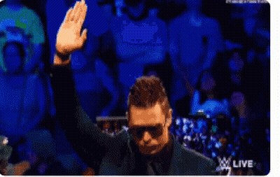 A Man Wearing Sunglasses Is Waving His Hand In Front Of A Crowd GIF