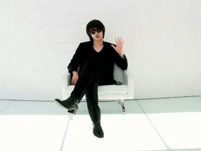 A Man Wearing Sunglasses Sits In A Chair With His Feet Crossed GIF